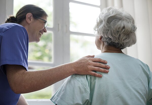 Pflegekraft legt einer Seniorin einfühlsam die Hand auf die Schulter und begleitet sie im persönlichen Gespräch.