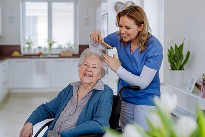 Pflegekraft kämmt einer Seniorin die Haare und unterstützt sie bei der täglichen Körperpflege.