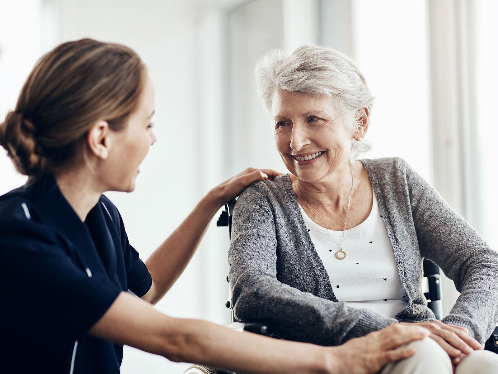 Pflegekraft spricht mit einer Seniorin im Rollstuhl und begleitet sie in einem persönlichen Gespräch.