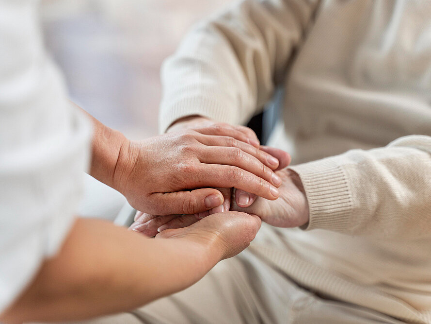 Pflegekraft hält die Hände einer älteren Person und vermittelt Nähe, Sicherheit und persönliche Zuwendung.