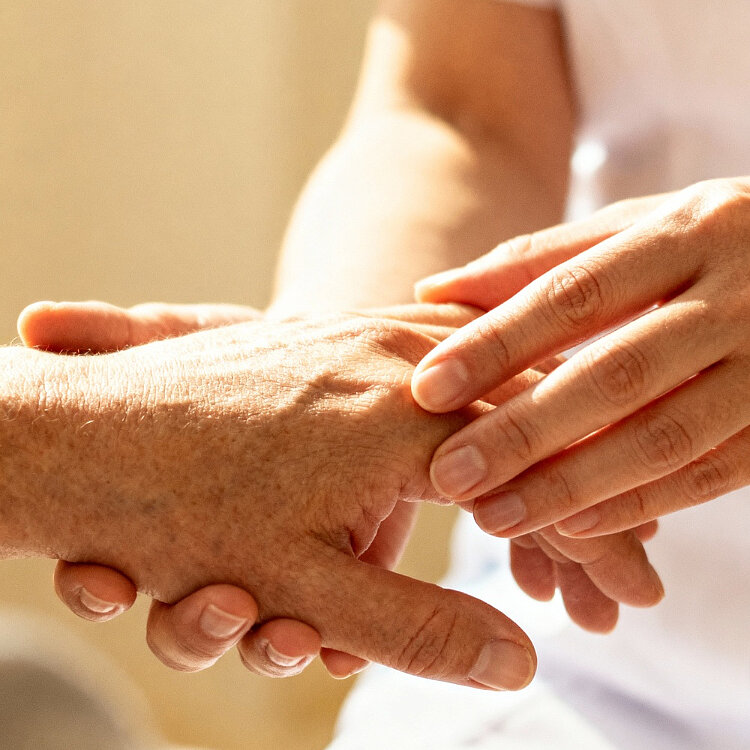 Pflegekraft hält einfühlsam die Hand einer älteren Person und spendet Halt und Unterstützung.