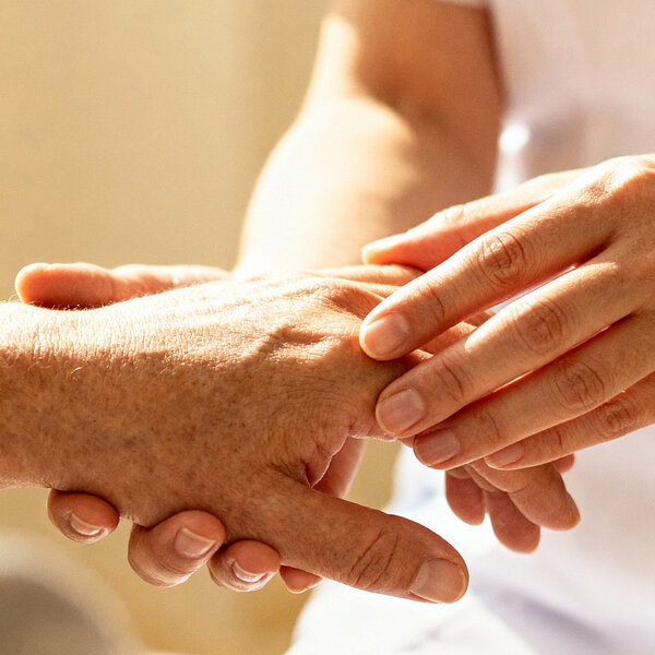 Pflegekraft hält einfühlsam die Hand einer älteren Person und spendet Halt und Unterstützung.